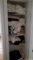 Closet shelves with neatly folded sheets, towels, and linens in white, beige, pink, dark blue, and gray colors.