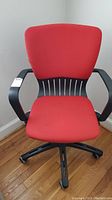 Front view of red fabric office chair with black armrests and five-legged base, showing the fabric and structure.