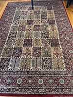 Full view of the area rug on hardwood floor showing the patchwork design and burgundy border.