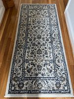 Top down image of one beige floral patterned entry hall rug on hardwood floor, showing entire rug and its floral design.
