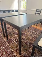 Black wood dining table positioned on a patterned carpet, showing the table top and four legs.