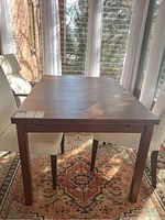 Full view of the extendable wooden dining table placed on a patterned rug near a window showing general condition and style.