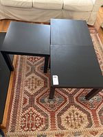 Three black square side tables arranged on a patterned rug in front of a beige sofa, showing size and condition.
