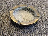 Top view of bronze colored aluminum ashtray with ash residue inside and four cigarette rests