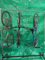 Front view of metal rolling bike rack with three bicycles hanging by frames, green tarp background