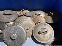 Top view showing multiple cast iron pot lids with integrated handles, displaying rust and grime