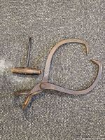 Antique fisherman's hook with wooden handle lying flat next to iron ice block tongs on textured fabric surface.