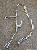 Full view of the industrial kitchen faucet laid flat on carpeted floor showing the extended arm, coil spring hose, spray nozzle, and supply lines.