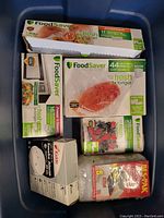 Top view of blue bin containing assorted FoodSaver freezer storage bags and a Kidde fire detector box.