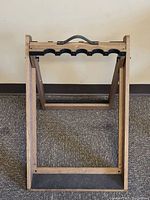 Full front view of the folded wooden rifle rack showing the carved slots for rifles and handle on top.