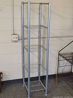Full view of the silver metal corner shelf unit showing its height and five wire grid shelves.