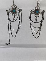 Pair of sterling silver dangling earrings with turquoise stone centers and multiple blackened silver chains. One earring shows a long loose chain detached and tangled.
