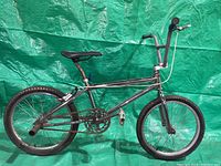 Side view of the entire silver BMX bike showing frame, tires, seat and handlebar against green backdrop.