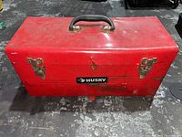 Closed red Husky metal toolbox with black plastic handle and brass latches.