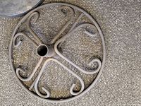 Metal umbrella stand with decorative scrollwork circular base and central tubular holder, showing dust and need for cleaning.