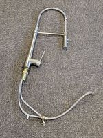 View of the entire chrome pull down kitchen faucet laid flat showing spring coil, spray head, lever handle, and two attached braided supply hoses.