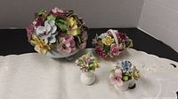 Four ceramic flower baskets with detailed multicolored pansies and leaves on a soft cream cloth, showcasing the lot contents