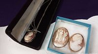 Necklace pendant in box with silver-tone chain and two cameo brooches in a blue box
