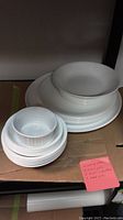 Stack of 8 dinner plates, 5 larger bowls, 5 smaller bowls stacked on a cardboard surface