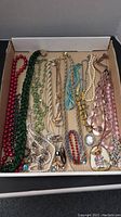 Wide view of assorted necklaces and pendants in box, showcasing variety of colors and materials.