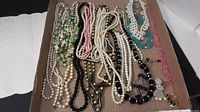 Overview of assorted necklaces in a box showing multiple colors and styles including faux pearls, beads, and chains.