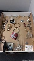 Various bracelets, necklaces, pins and more arranged in a cardboard box, some in cases or plastic bags