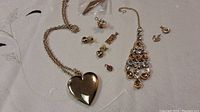 Photo of gold coloured costume jewellery including heart pendant necklace, earrings and other small jewelry pieces displayed on fabric.