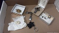 Photo showing large cross brooch or pendant in case, several rings, small pads with a compact round brooch and turtle clip-on brooch, black carved flower pendant or keychain.