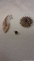 Three pieces displayed together: leaf brooch with pearls, sunburst brooch, garnet pendant