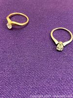 Two rings displayed on purple cloth: one white gold and one yellow gold ring.