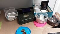 Various small jewelry boxes and clear plastic containers with lids, placed on a table surface.