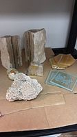 Pair of rough natural stone bookends, white carved stone cluster, hexagonal coasters stacked, and polished stone egg on cardboard surface.
