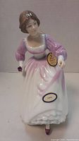 Front view of the Royal Doulton Ashley figurine showing the full dress and a tag attached indicating authenticity.