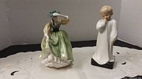 Two Royal Doulton porcelain figurines: Darling HN 1319 and Buttercup HN 2309, about 7 inches high, shown on a lace cloth background with neutral backdrop.