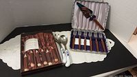 Photo showing boxed set of 6 steak cutting utensils with brown handles, pair of white porcelain salad servers with blue floral pattern, and box of 6 dessert forks with brown handles.