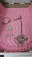 Four piece sterling silver filigree jewelry set shown on pink fabric: bracelet, round floral pin, bow-shaped pin, and necklace with pendant.