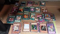 Top view of approximately 50 Yugioh trading cards, showing a mix of monster, spell, and trap cards with different designs and colors spread out on a flat surface.