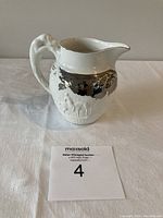 White Wedgwood creamer with silver accent and hound handle shown from front angle on white background.