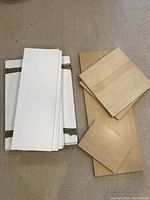 Stacked white and wood grain laminated particle board shelving panels viewed face up on carpet, showing size and finish variation.