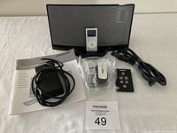 Photo of Bose SoundDock digital music system with iPod docked, power cord, remote control, power adapter, and instruction manual all laid out on a white surface.