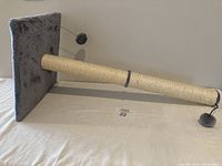 Side view of gray fabric covered square base supporting long sisal rope wrapped scratching post with two hanging plush balls attached by springs on each end.
