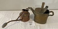 Two small metal watering cans displayed side by side, one copper on left and one brass on right