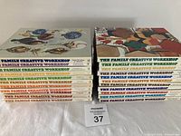 Two stacks of 21 hardcover handicraft books from the Family Creative Workshop series, showing colorful illustrated spines and covers.