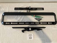 TV wall bracket parts including main mount frame, secondary bar, tilt mechanism, and mounting hardware laid out on a white surface.