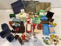 Overview of assorted vintage dollhouse furniture painted in various colors, with miniature sofas, chairs, tables, bathtub, and cabinet pieces along with six dolls and small rugs.