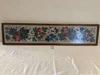 Full view of the framed needlepoint floral artwork showing the entire horizontal composition and wooden frame.