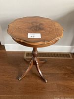 Front view of the round scalloped edge wooden pedestal table on hardwood floor showing the full table shape and legs.