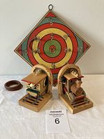 Full view of ring toss set with the Chad Valley ring toss board in the background, two wooden train bookends in front on a table, and four wooden quoits on the left side.
