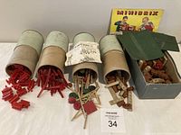 Toys including red plastic connectors in cylindrical containers, loose wooden sticks and wheels, and boxed Minibrix pieces.