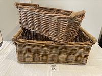 Two wicker baskets shown stacked, smaller basket resting inside larger basket, on white surface